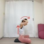 あぐらで座り、頭の後ろで両手を組み、背筋を伸ばして頭を前に倒す首の後ろのストレッチ