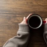 ホットコーヒーを両手で持つ女性の手元