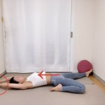 左膝を曲げた半分の割座から仰向けになり両手を頭上に伸ばし、右手で左手首をつかんだ体勢、