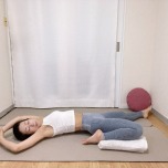 左膝を曲げた半分の割座から仰向けになり、膝下にタオルを挟み、膝の負担を軽減して行うストレッチ