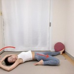 左膝を曲げた半分の割座から仰向けになり両手を頭上に伸ばし、右手で左手首をつかんで上体を左に傾けたストレッチ
