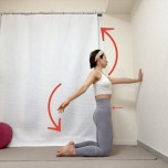 壁に向かって膝立ちになり、片手を壁に、もう片方の腕を大きく回す肩こり解消エクササイズ