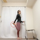 椅子の背もたれに右手を添え、左膝を曲げて脚の甲を掴んで立った体勢