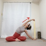 あぐらでタオルの両端を持ち、右手を床に下し、左肘を伸ばして上体を右に傾け、左わき腹を伸ばすストレッチ