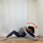 脚を広めに開いて膝を立てて座り、背骨を緩めて前屈した体勢から上体を右にスライドしたストレッチ