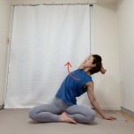 左肘を曲げて高く引き上げ、腕を耳の横に近づけて脇を大きく開いてあぐらで座り、胸を天井に見せるようにして背骨を軽くひねって脇を開くストレッチ