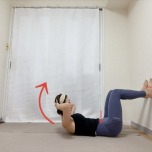 脚の裏を壁につけて膝を曲げた仰向けから上体を床から小さく浮かせる腹筋のエクササイズ