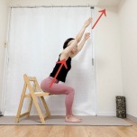 椅子に座り、背筋を伸ばしたまま上体を前に傾け、両腕を斜め上に伸ばした体勢