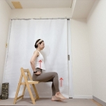 両手を腰に添え、背筋を伸ばして椅子に座り、片脚を床から少し浮かせた体勢