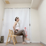 両手を腰に添え、背筋を伸ばして椅子に座り、片脚を床から少し浮かせて上下に動かすトレーニング