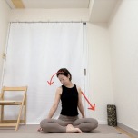 右腕を斜め後ろの床へ伸ばしたあぐらで座り、頭を左斜め下へ傾け、右の首筋から肩まわりを伸ばすストレッチ